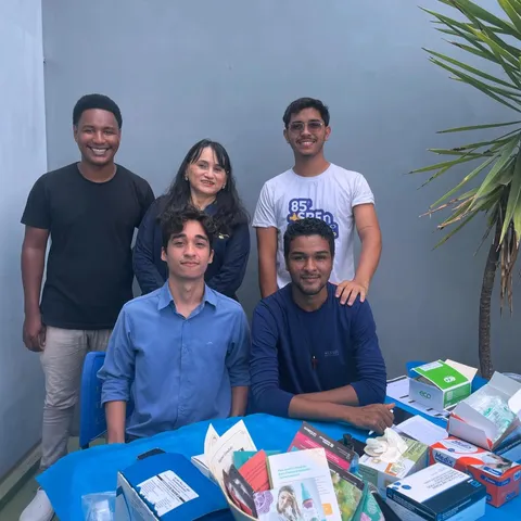 Jovens posam atrás de uma mesa com materiais de saúde.