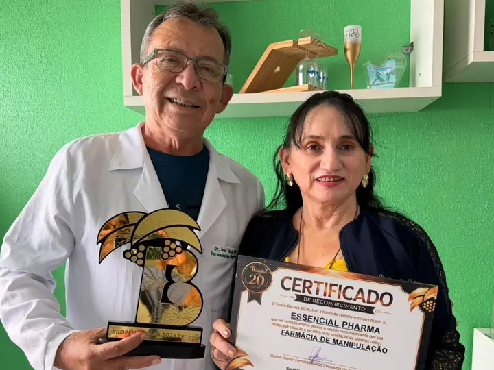 Um homem de jaleco e uma mulher posam com uma estatueta dourada e um quadro com o nome da Essencial Pharma.