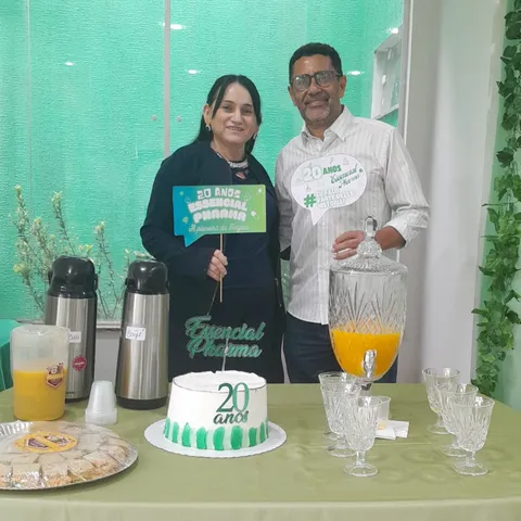 Uma mulher e um homem seguram plaquinhas atrás de uma mesa com bolo, suco e copos.