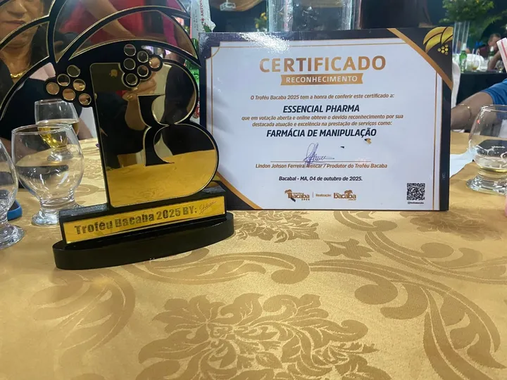 Uma estatueta dourada e um quadro com o nome da Essencial Pharma, sobre uma mesa.