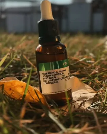 Um frasco conta-gotas com o rótulo da Essencial Pharma sobre a grama, ao sol.